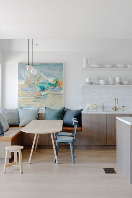 a serene coastal kitchen with whitewashed cabinets, open shelves and a cozy dining zone with blue pillows in the corner