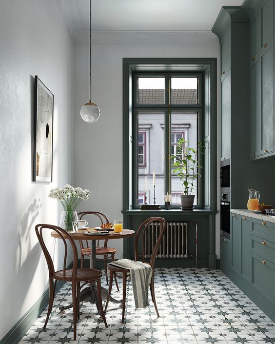 a small and pretty Scandi kitchen with dark green cabinets, a printed tile floor, vintage dining set and some chic decor