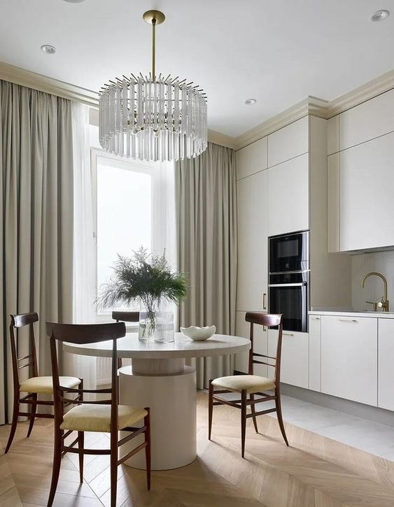 a sophisticated neutral eat-in kitchen with creamy cabinets, a round table, rich-stained chairs and a crystal chandelier