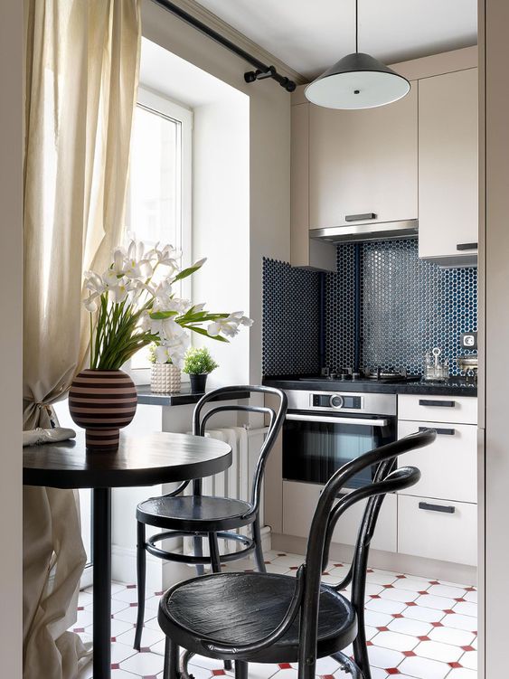 a tiny functional kitchen with tan cabinets, a navy penny tile backsplash, a small dining set in black in the corner