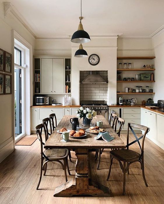 a vintage creamy farmhouse kitchen with butcherblock countertops, a vintage stained dining set and black pendant lamps