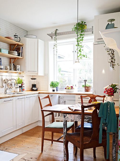 an airy Scandi kitchen with white cabinets, open shelves and a stained vintage dining set plus greenery