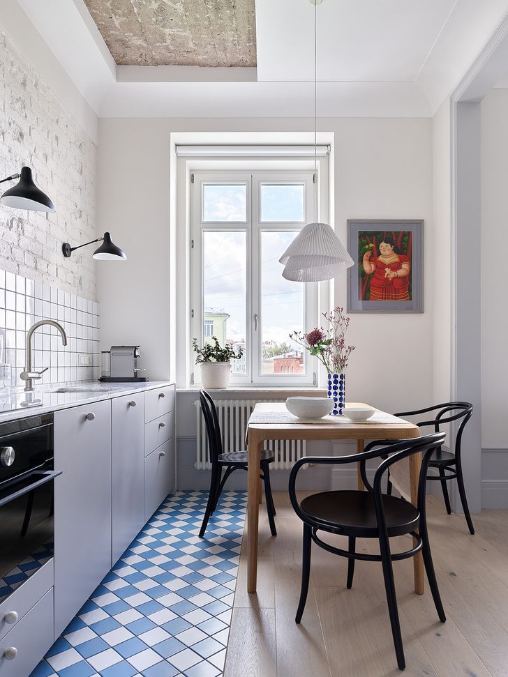 an airy Scandinavian kitchen with grey lower cabinets, a transitional floor from tiles to laminate, a table and black chairs
