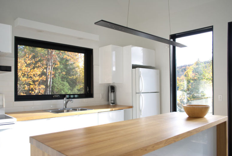 The kitchen is done with white cabinets and a kitchen island and is covered with light-colored wood countertops, there are windows everywhere
