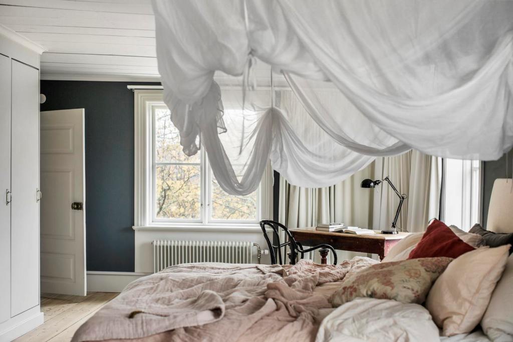 The master bedroom is a peaceful space with a large bed with a suspended canopy and a desk byt the window