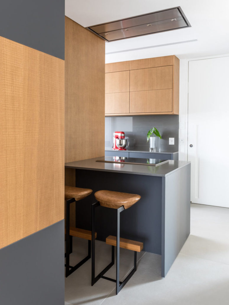 The kitchen features sleek grey surfaces and wood for a contrast, there's a kitchen island with a breakfast nook