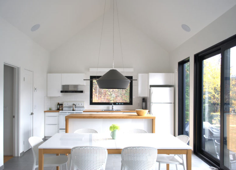 The dining space is done with a white dining table and chairs and is marked with a graphhite grey pendant lamp