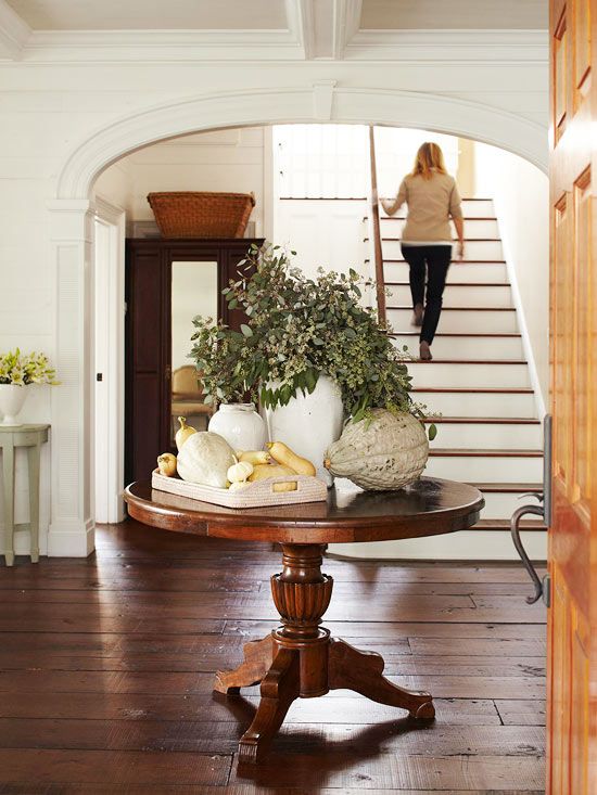 a large console table with fresh greenery in a vase, a wooden tray with pumpkins and gourds and an oversized pumpkin