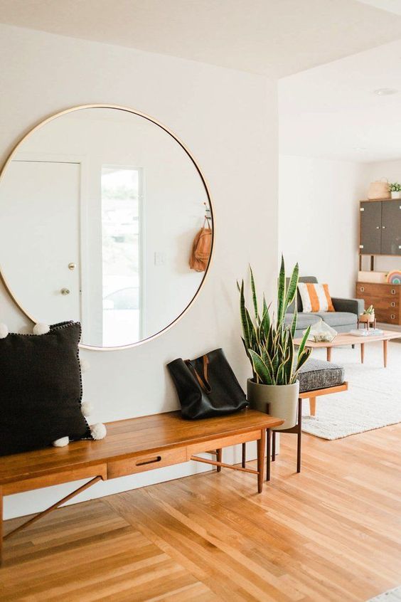 an airy mid century modern entryway with an oversized round mirror and a cool bench