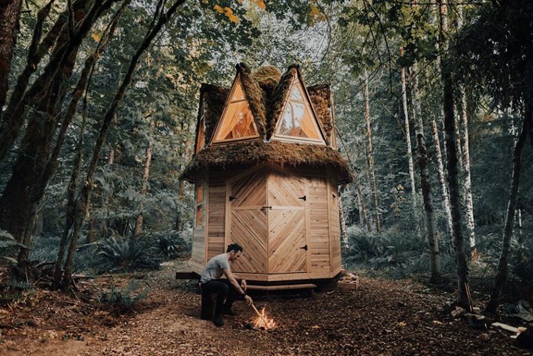 The cabin is placed outside and the owners may make a fire next to it and sit on tree stumps