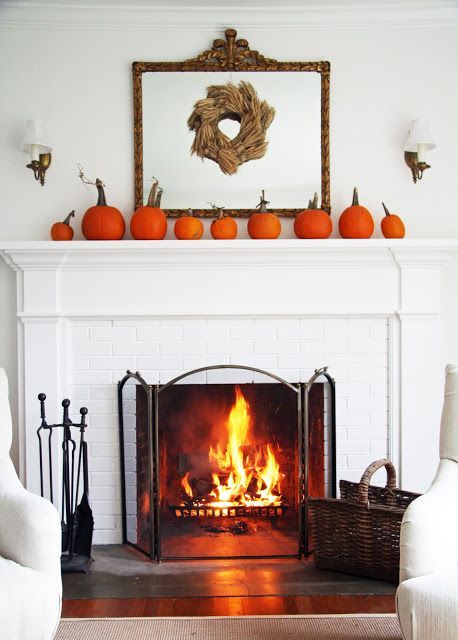 a simple rustic mantel with an arrangement of orange pumpkins and a wheat wreath on the mirror