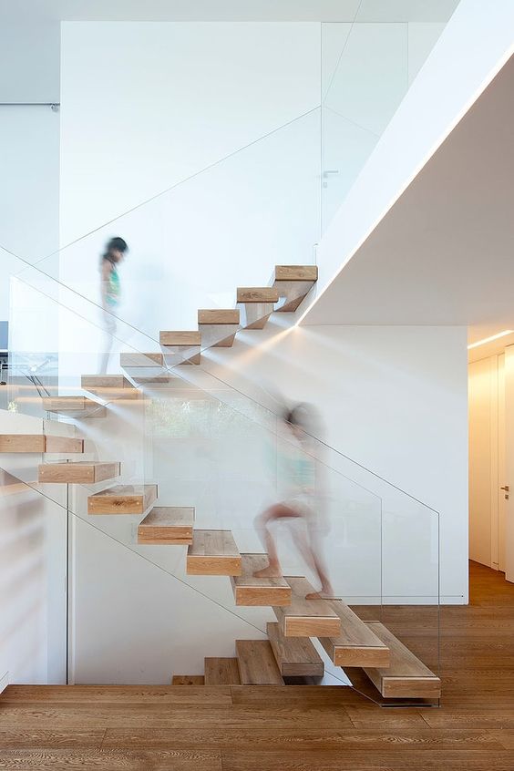 a floating staircase made of wood and with glass railing that holds the steps at the same time