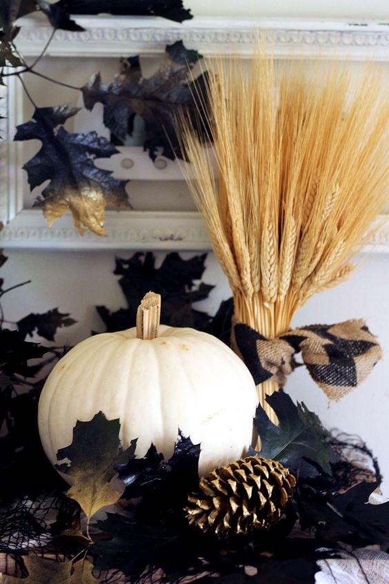wheat, a white pumpkin, a gilded pinecone and some fake black leaves create a dramatic arrangement for Halloween