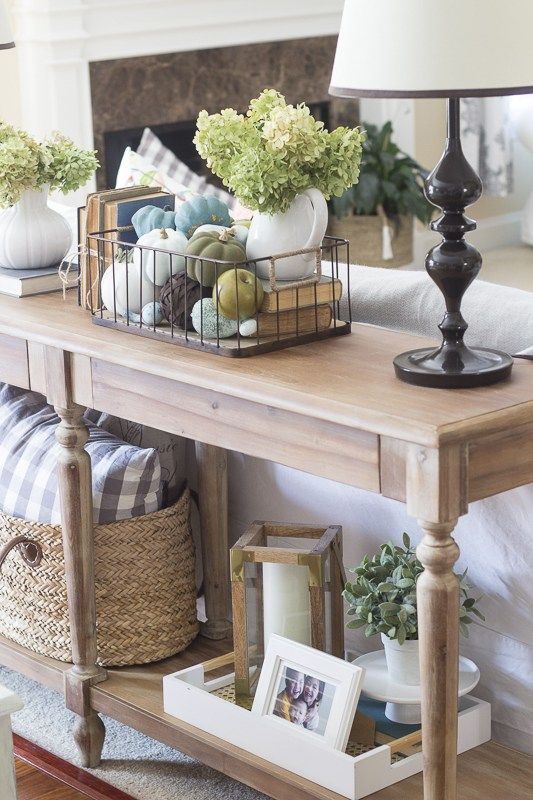 a vintage console with a wire basket with fake pumpkins, fresh hydrangeas and some candle lanterns