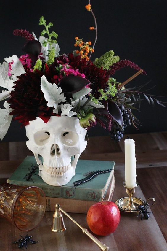 a skull vase with a moody and textural floral and greenery centerpiece with burgundy and plum touches