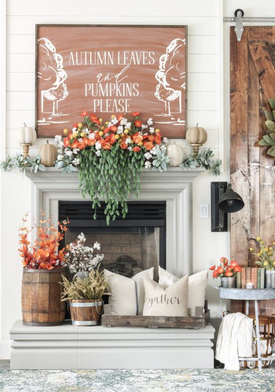 a fall mantel with lush flowers and greenery, fake pumpkins and a large artwork over it