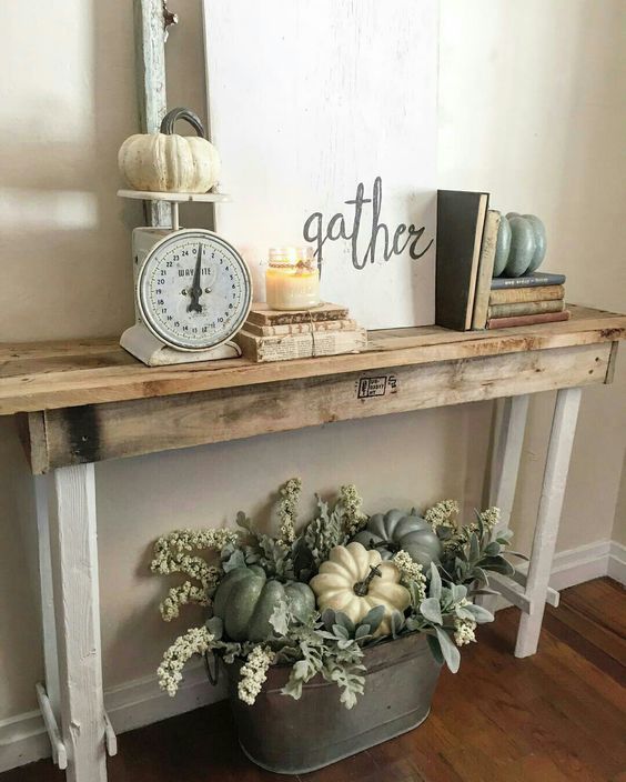 an industrial console with vintage scales, a candle, a sign and a metal bucket under the console with fake greenery and pumpkins