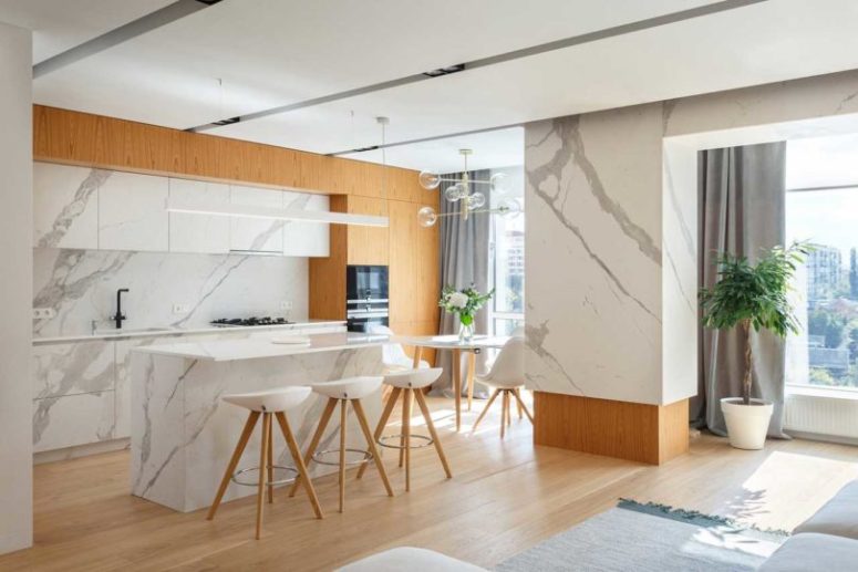 The kitchen is done with light-colored wooden cabinets and stone-inspired surfaces, there's a kitchen island with a breakfast space