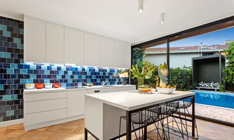 The kitchen is done with white cabinets and a large kitchen island with an eating space and a navy and blue tile backsplash