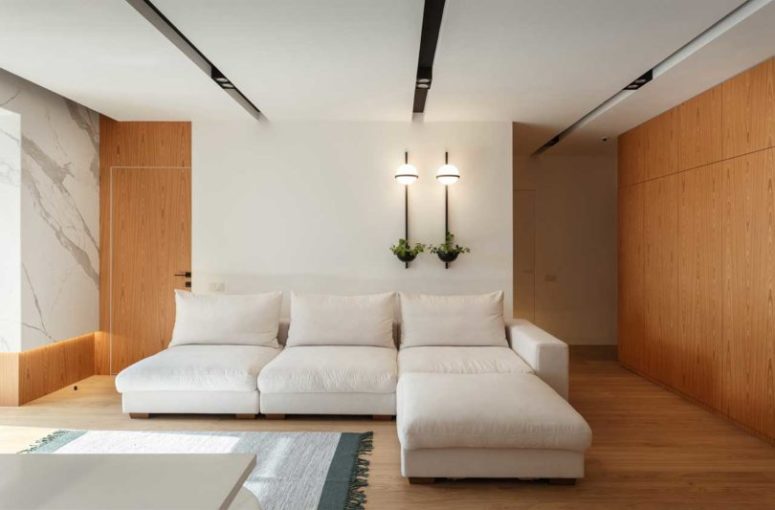 The living room is airy and light-filled, with a large sofa and wall lamps