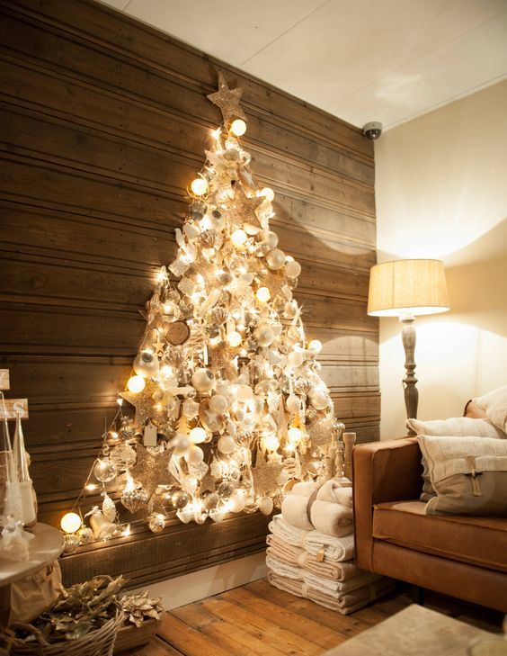 a shiny wall-mounted Christmas tree made with lights on the contour and with lots of silver, pearly and white ornaments inside