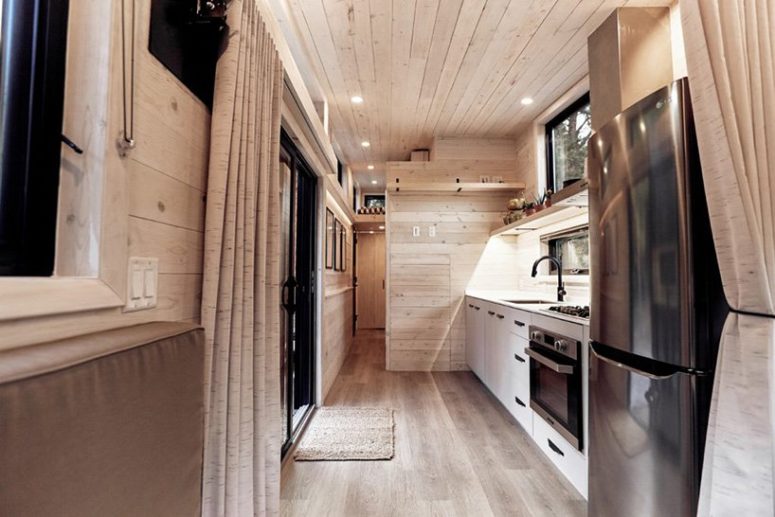 The kitchen is also clad with whitewashed pine, there are cabinets, a fridge, a cooker and some shelves plus window backsplashes