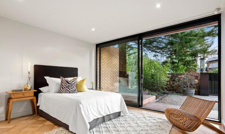The master bedroom features a comfy bed, several bedside tables, a contemporary chair and a glazed wall with an entrance to the garden