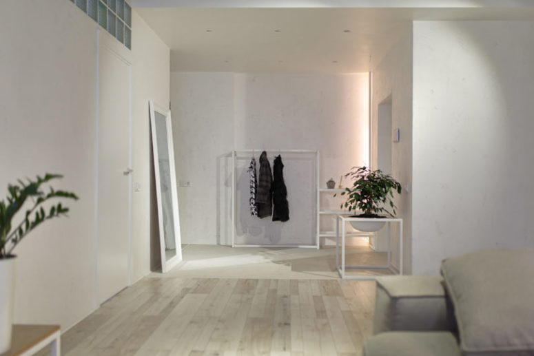 The entryway shows off a large mirror, a clothes hanger and a large planter in a stand, ambient lights are enough here