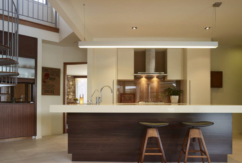 The kitchen is done with white cabinets, a dark kitchen island with a white top and a bold glass backsplash