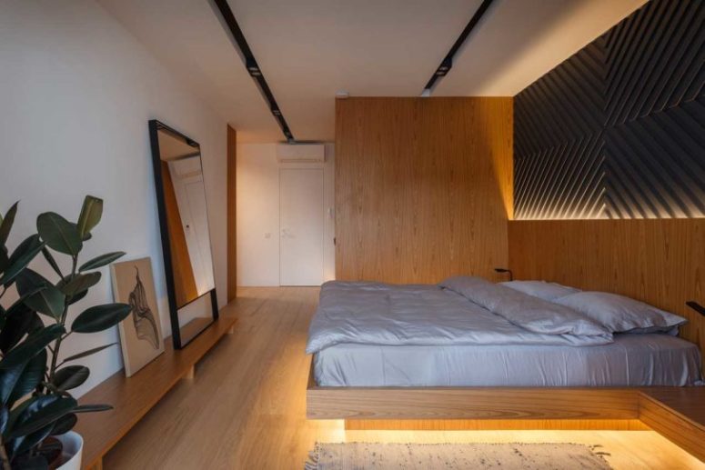 The master bedroom is done with light-colored wood, a platform bed with lights and a geometric artwork