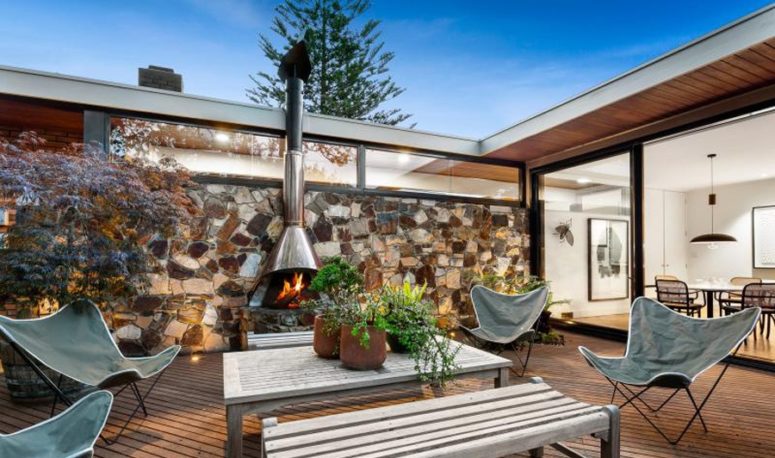 This outdoor space is done with several leather chairs, wooden benches and tables and a hanging hearth