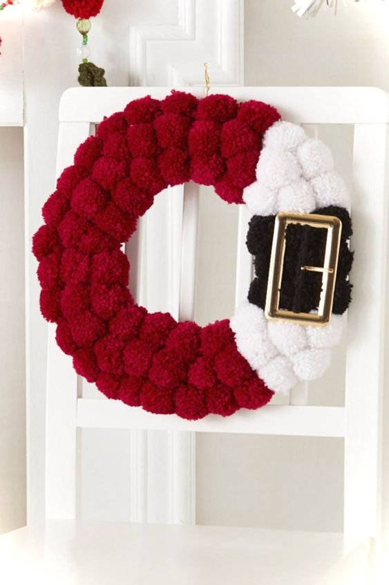 a red, black and white pompom Santa inspired wreath with a large buckle is a fun idea instead of a usual greenery one a red, black and white pompom Santa-inspired wreath with a large buckle is a fun idea instead of a usual greenery one