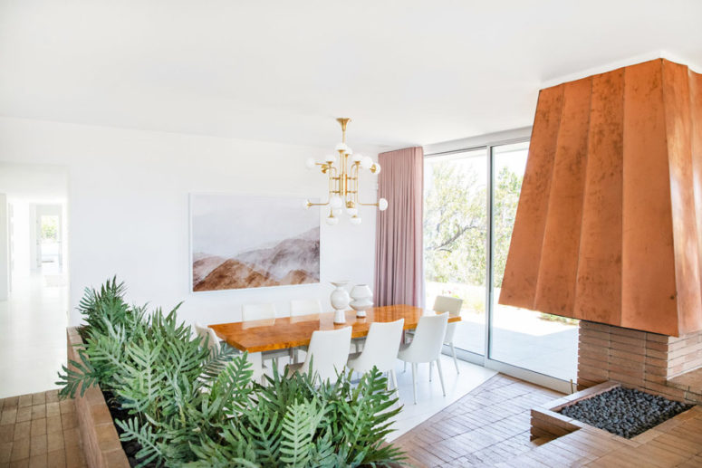 The dining zone is done with a fireplace with a bold hood, a dining table and white chairs