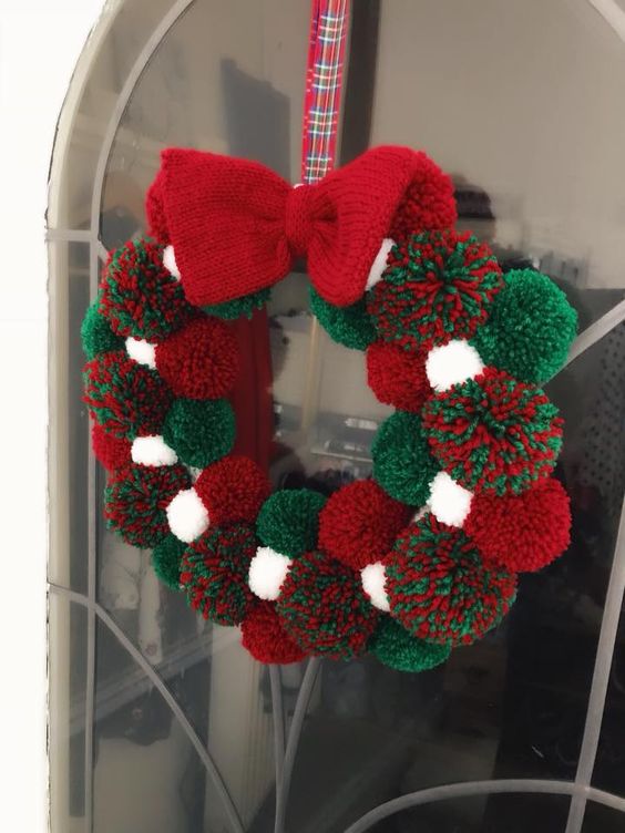 a Christmas pompom wreath of white, green and red pompoms and a knit bow