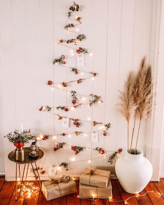 a boho wall-mounted Christmas tree of lights, berries and Christmas cards plis pampas grass and blooms around