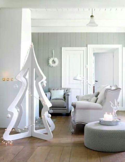 a cutout plywood white Christmas tree decorated with lights and some ball ornaments