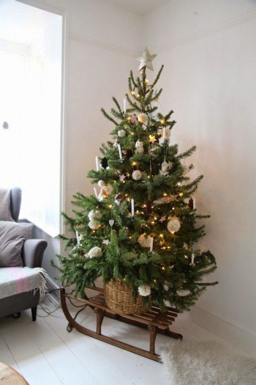 a simple rustic Christmas tree decorated with white pompoms, candles, stars, lights and cookie ornaments plus a basket and a sledge