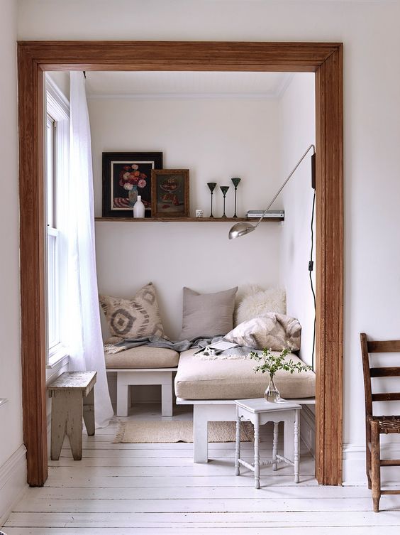 an L-shaped bench with upholstery, a couple of shabby side tables, a shelf and a sconce