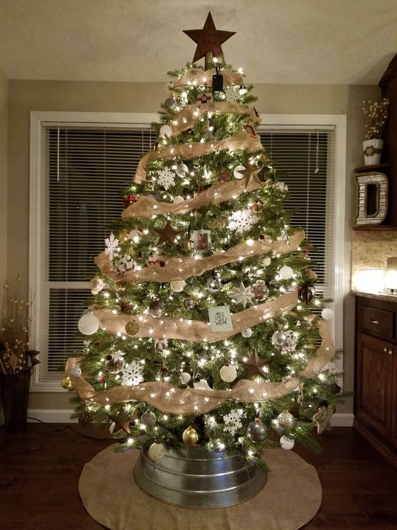 a cozy rustic tree with burlap ribbons, a wooden star on top, metallic ornaments and pinecones and a galvanized tub as a cover