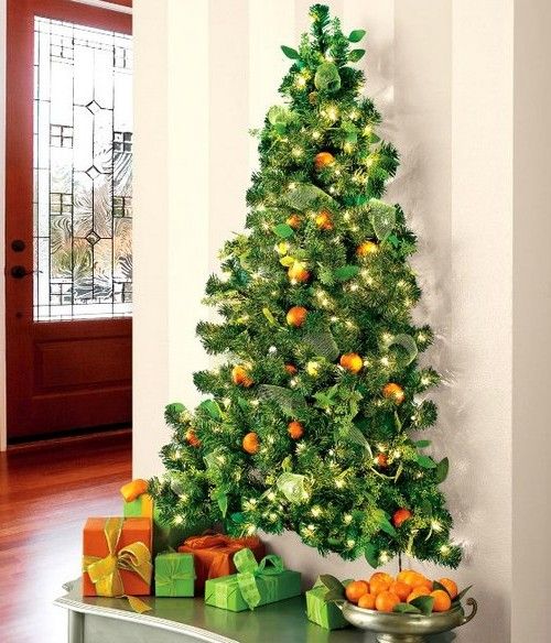 a small wall-mounted Christmas tree realized with evergreens, lights, pinecones and real tangerins