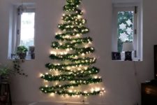 16 a wall-mounted Christmas tree silhouette done with an evergreen garland and lights for a modern space