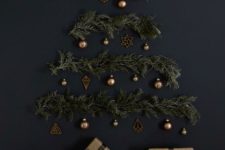 17 a stylish wall-mounted Christmas tree on a black wall of evergreens, lights and brass ornaments
