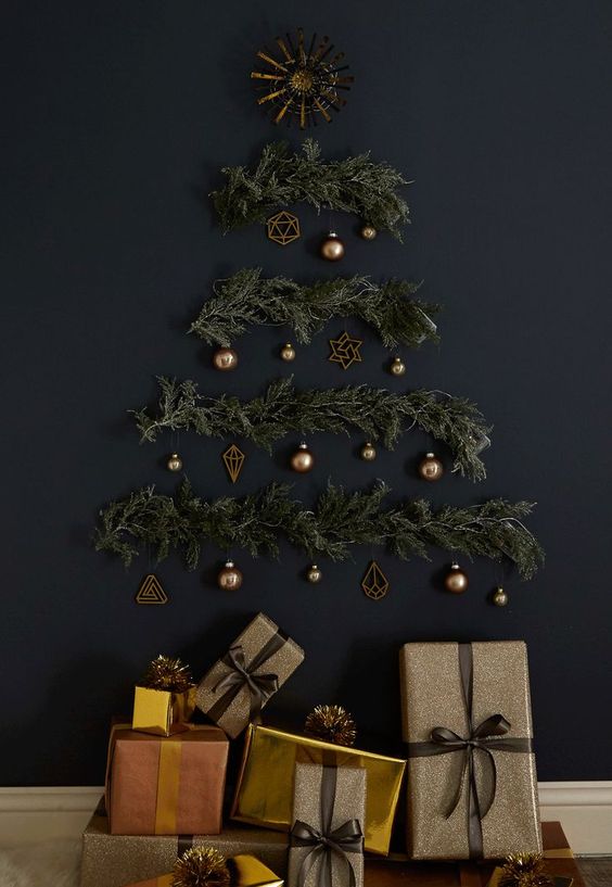 a stylish wall-mounted Christmas tree on a black wall of evergreens, lights and brass ornaments