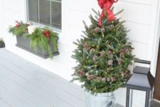 22 a small holiday tree decorated with lights, pinecones and a red bow on top in a galvanized bucket for a porch