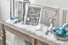 24 a snowy console with fake snow, ornaments, lanterns, signs and a fake deer for a cozy and cool Christmas look