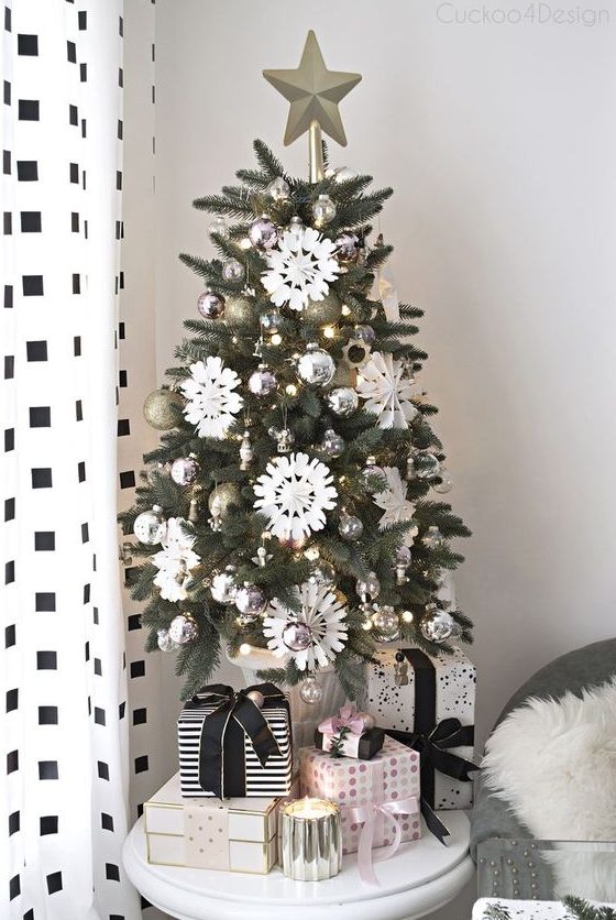 a chic and shiny tabletop Christmas tree with lights, silver and gold glitter ornaments, white paper snowflakes and a star topper