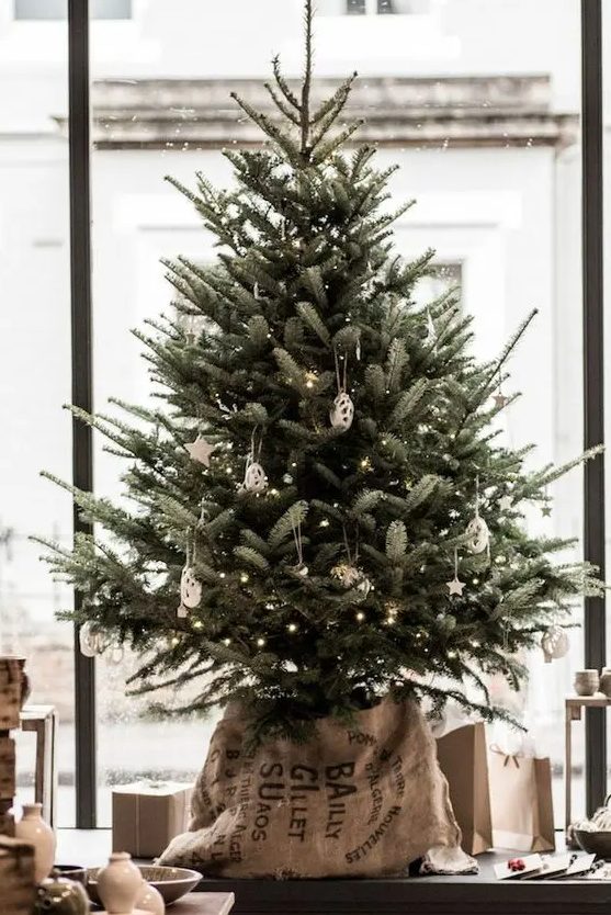 a delicate tabletop Christmas tree decorated with lights, white clay ornaments and put into a sack for a slight industrial feel