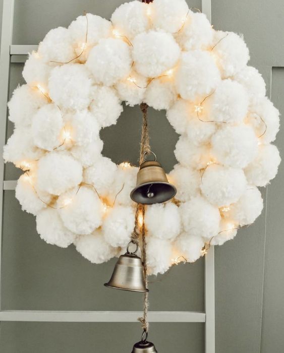 a heavenly beautiful white pompom Christmas wreath with lights and large bells is a cool winter or Christmas decor idea