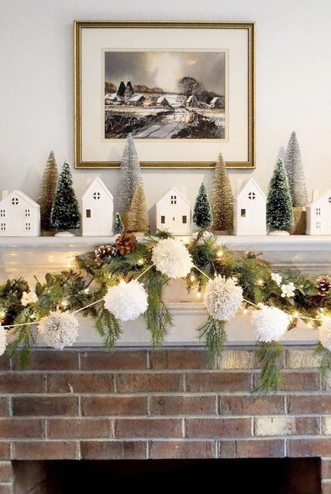 a lovely Christmas mantel with an evergreen and pinecone garland, a pompom one, lights, bottle brush trees and houses
