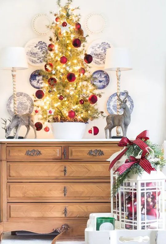 a lovely tabletop Christmas tree with lights, tiny star and large red ornaments and pinecones in the bowl is amazing